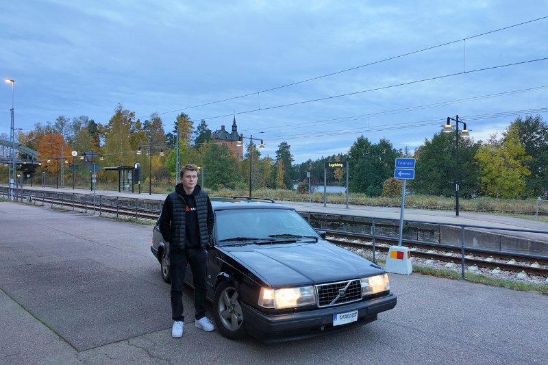 En kille står brevid sin gräna epa, volvo. Precis vid spåret nära tåget.